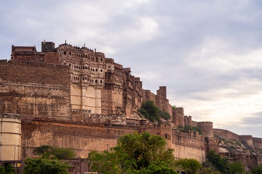 majestic stone walls of mehrangarh fort with window arches in jodhpur sitting on top of hill surrounded by monsoon clouds with birds flying around this landmark of rajput warrior history India