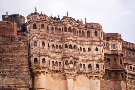 majestic stone walls of mehrangarh fort with window arches in jodhpur sitting on top of hill surrounded by monsoon clouds with birds flying around this landmark of rajput warrior history India