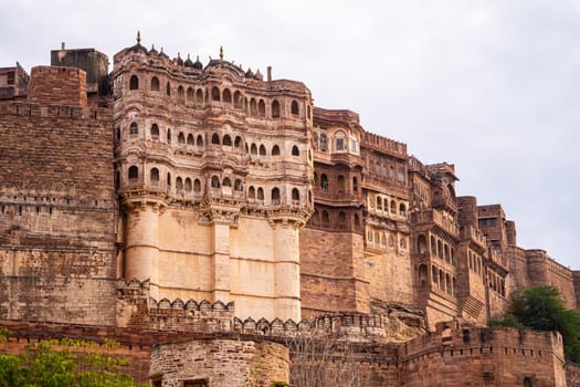 majestic stone walls of mehrangarh fort with window arches in jodhpur sitting on top of hill surrounded by monsoon clouds with birds flying around this landmark of rajput warrior history India