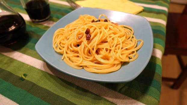 A plate of spaghetti carbonara ready at the table with a quarter of red wine.