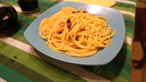 A plate of spaghetti carbonara ready at the table with a quarter of red wine.