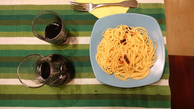 A plate of spaghetti carbonara ready at the table with a quarter of red wine.