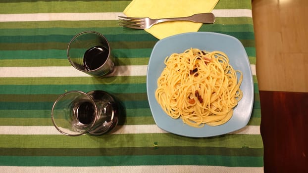 A plate of spaghetti carbonara ready at the table with a quarter of red wine.