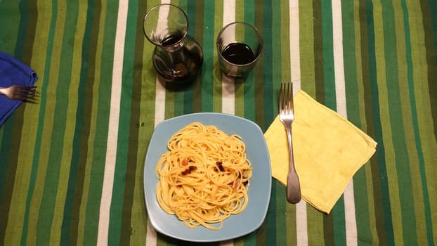 A plate of spaghetti carbonara ready at the table with a quarter of red wine.