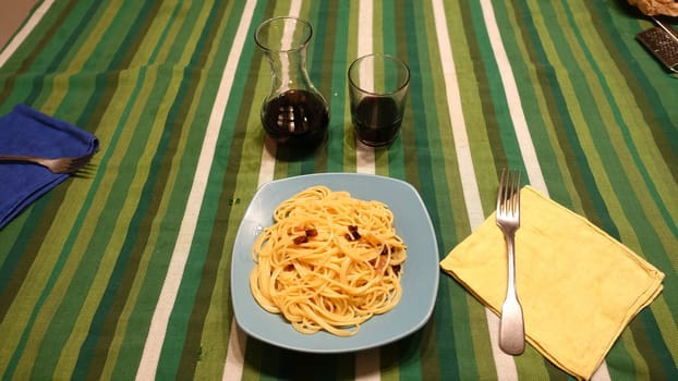 A plate of spaghetti carbonara ready at the table with a quarter of red wine.