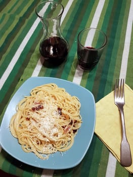 A plate of spaghetti carbonara ready at the table with a quarter of red wine.