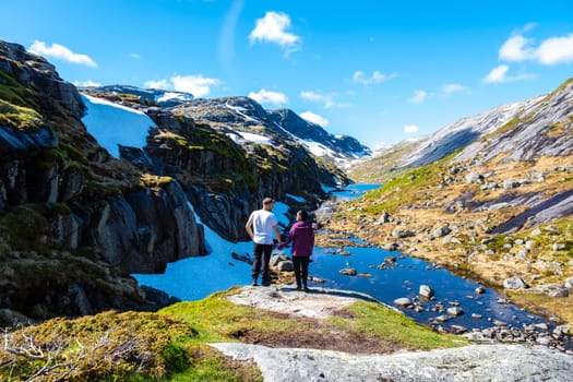 A couple stands on a rocky outcrop overlooking a serene glacial lake in Norway. Kjeragbolten Norway