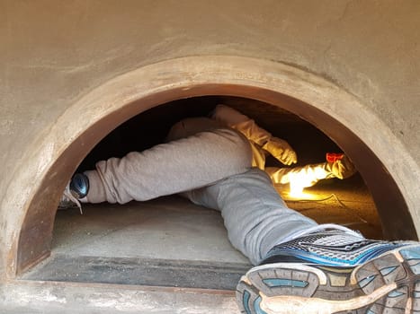 The feet and legs of a person cleaning the inside of a pizza oven during construction.