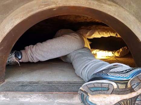 The feet and legs of a person cleaning the inside of a pizza oven during construction.