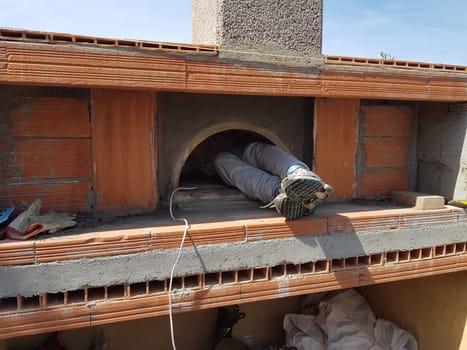 The feet and legs of a person cleaning the inside of a pizza oven during construction.