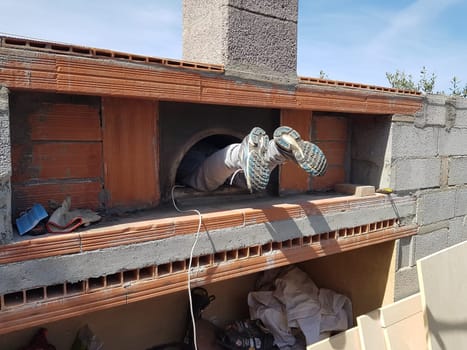 The feet and legs of a person cleaning the inside of a pizza oven during construction.