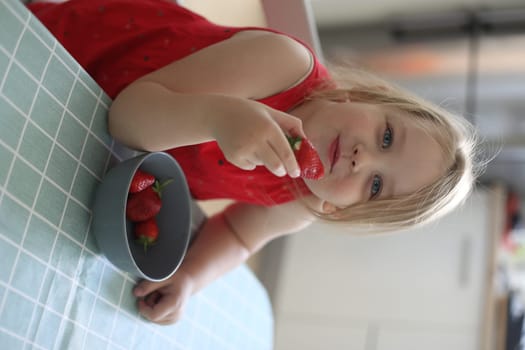 happy child girl eats strawberries in the summer home kitchen. Child enjoys a delicious berry