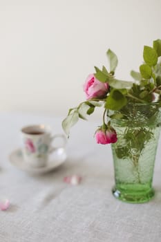 Moody summer still life. Table composition with cup of coffee, tea and beautiful floral bouquet with pink roses.