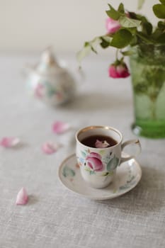 Moody summer still life. Table composition with cup of coffee, tea and beautiful floral bouquet with pink roses.