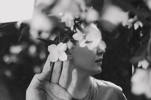Abstract contemporary art collage black and white portrait of young woman with flowers on face hides her eyes. Creative portrait with Multiple exposure.Young beautiful female model with flowers