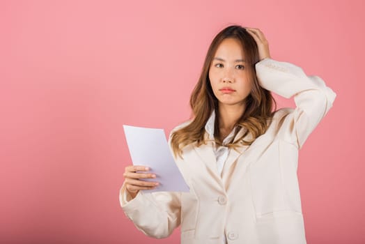 Portrait of beautiful Asian young woman sad tired strain holding paper calculating bills on hand, female person problem she hold worried over bill, studio shot isolated on pink background
