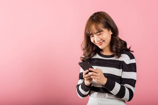 Happy Asian portrait beautiful cute young woman teen smiling excited using smart mobile phone studio shot isolated on pink background, Thai female surprised making winner gesture on smartphone