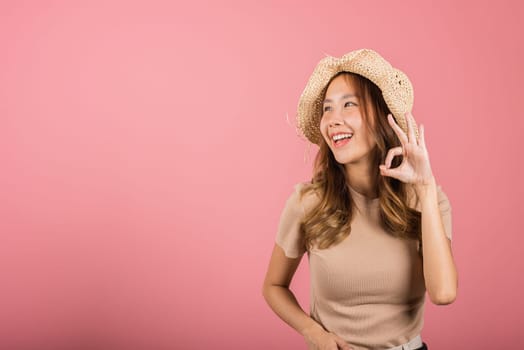 Portrait Asian young woman is smiling with hat holding her hand up in the air, giving the OK sign in studio shot isolated pink background, which gives it a cheerful and positive vibe, excellent sign