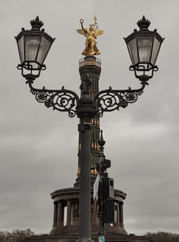 Berlin, Germany - Dec 20, 2023 - The victory column with historical street lamp in foreground. The Victory column with Goddess Victoria to Celebrate Prussia's victory in the Franco-German War in the Tiergarten, One of the most important sights of Berlin and one of the most important national monuments of Germany, Space for text, Selective focus.