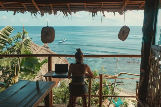 Woman sitting at table with laptop in front of ocean view, inspirational remote work environment with travel vibes