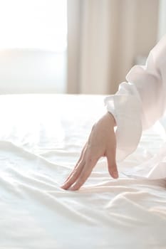 Woman Hand touching bed sheets, closeup. Young woman intimacy on bed. Soft, gentle, tender cozy morning concept