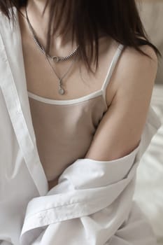 Close-up of Young woman in lingerie and white shirt sit on bed indoors at home in the morning after waking up, back view. Relaxing , Cozy, good morning, comfort, intimacy concept