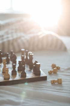 Chess board in sunlight on bed. Strategy thinking. Morning ideas concept. Pastel shades. Unmade bedding sheets and blanket.