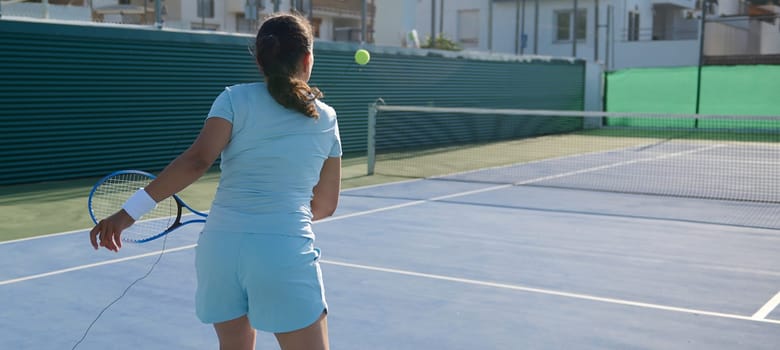 A woman in her 40s playing tennis on an outdoor court on a sunny day. She is about to hit the tennis ball, focusing on her game and enjoying an active lifestyle.