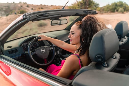 A woman is driving a red convertible with her hair in a ponytail. She is wearing a pink dress and is smiling