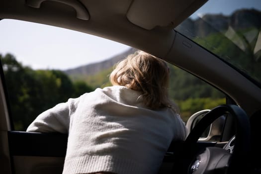 A blonde woman in a white sweater and jeans is driving. Happy woman sitting in the car