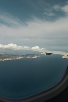 A beautiful view of the wing of an airplane and an island in the sea through the porthole window from the height of an airplane in the evening at sunset, close-up side view.