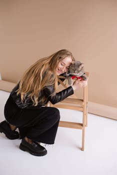 A woman natural blonde long hair smiling in a black clothes sitting on photo studio. girl with pet scottish straight cat. portrait , vertical, close up