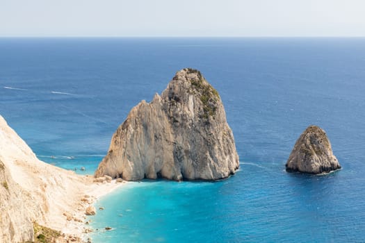 Beautiful view of two rocks in the blue sea with boats sailing in the distance near the beach coastline on a summer sunny day, side view close up.