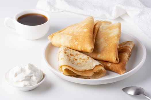 Pancakes with sour cream on a white table.