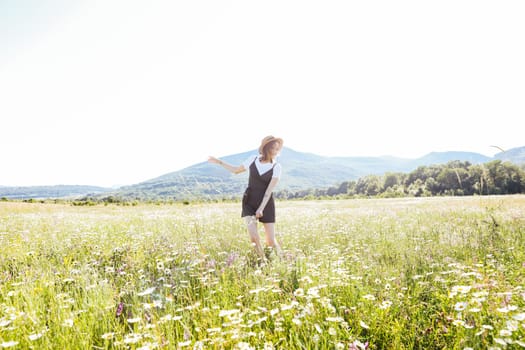 a woman in straw hat walks in a field with daisies flowers in nature