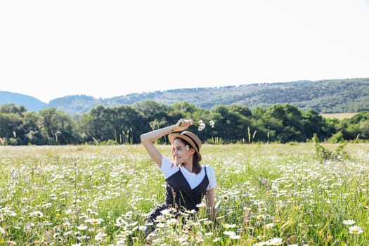 in nature, woman in a straw hat sits in a field with daisies flowers