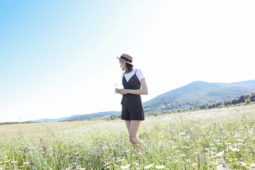 woman in a straw hat walks in a field with daisies flowers in nature