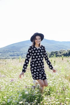 a woman in hat walks in a field with daisies in nature