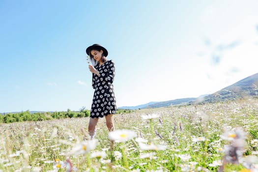 a woman in hat walks in a field with daisies in nature