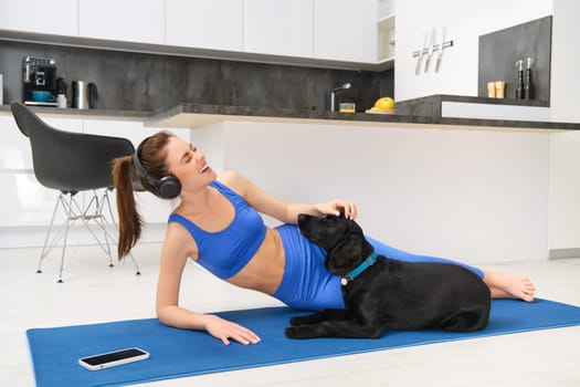 Lifestyle and fitness concept. Happy young woman doing aerobics while her dog wants to play, laughing and smiling, laying on yoga mat.