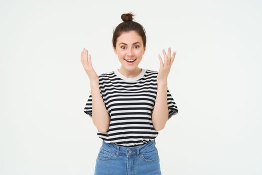 Image of excited girl clap hands, applause, looks surprised and happy, celebrates due to great news, stands over white background.
