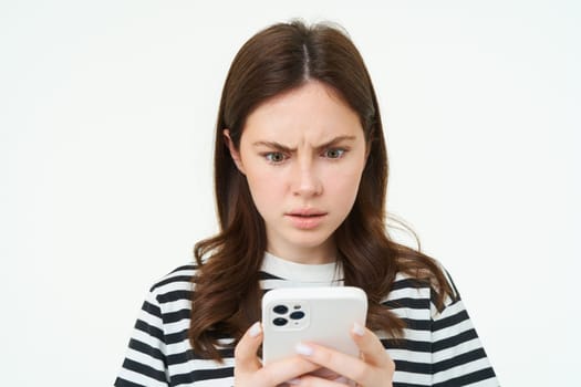 Woman looking confused and shocked at smartphone screen, frowning, reading upsetting, concerining news on mobile phone, isolated on white background.