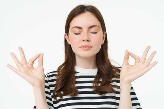Everything under control. Young woman meditating, standing in zen, yoga pose, keeps calm, posing with closed eyes, breathing with relaxed mindful expression.