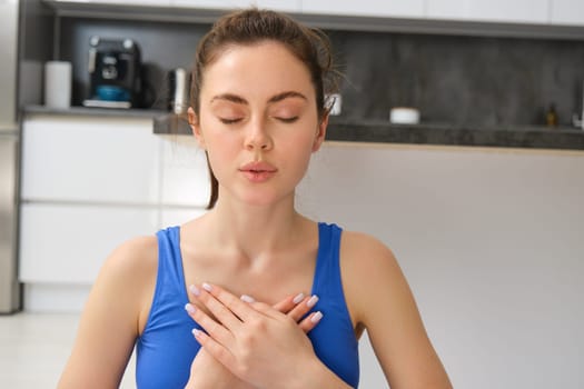 Woman practicing yoga and meditation at home sitting in lotus pose on yoga mat, relaxed with closed eyes. Mindful meditation concept. Wellbeing.