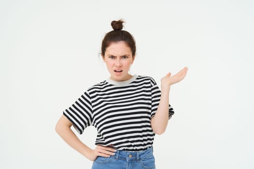 Portrait of angry woman complaining, raising one hand and shrugging looking frustrated, waiting for explanation, doesnt udnerstand smth, standing over white background.