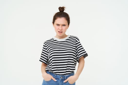 Image of bothered, disappointed young woman, frowning, complaining, looking angry and upset, standing over white background, arguing.