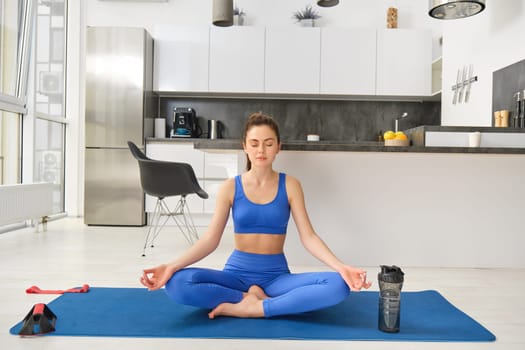 Fitness and mindfulness. Young woman doing yoga, sitting at home and meditating, close eyes and sits in asana pose on rubber mat.