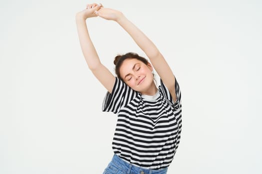 Image of beautiful girl stretching her arms with pleased, satisfied face expression, isolated against white background.