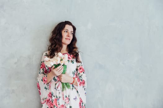 a woman in a floral dress with tulip flowers stands against a gray wall