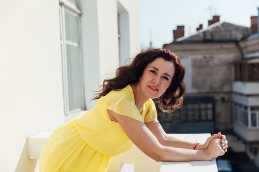 brunette woman in a yellow dress stands on the balcony of the room